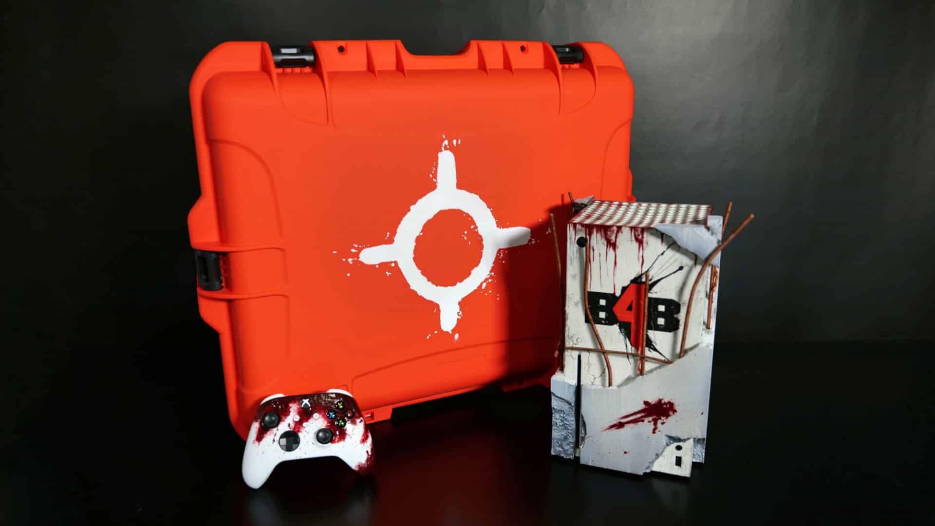 Aperçu de la console et manette Back 4 Blood, placées devant une caisse protectrice de couleur orange vif.