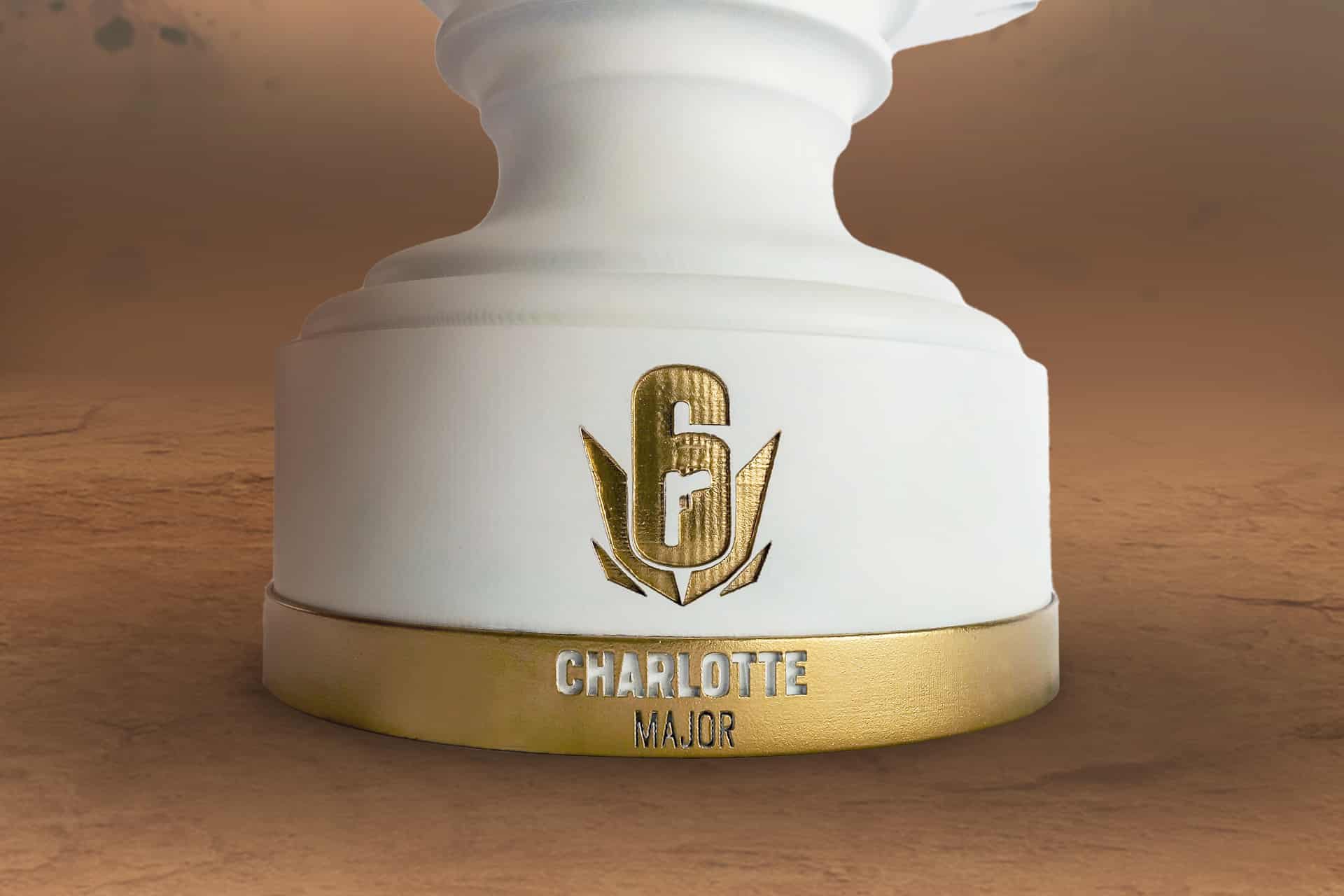 L'image présente le trophée Six Charlotte Major. Le trophée est en plan rapproché sur le bas / socle du trophée, présentant le logo du Six Charlotte Major, en détail gravé et doré sur fond blanc.